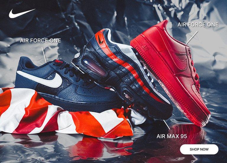 A Nike retail banner features a collage of sneakers in a red, white, and navy blue color scheme, set against a crinkled metallic silver background and striped fabric. The left side showcases a low-top navy blue Air Force 1 with a white Swoosh, a black Air Max 95 with red wavy overlays, and an all-red low-top Air Force 1. The right side mirrors these styles in a dynamic, overlapping arrangement, with a white Shop Now button in the bottom right corner.