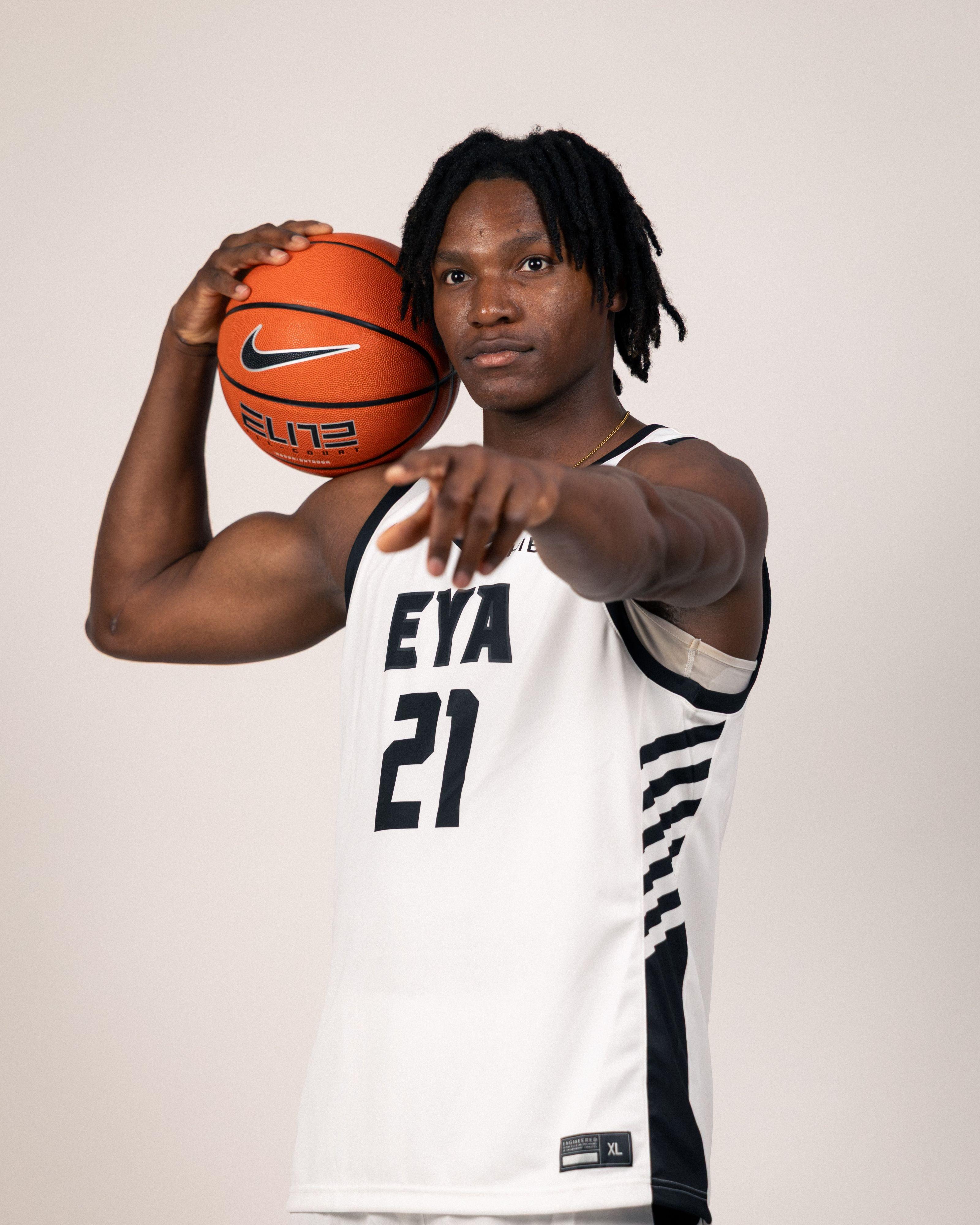 Basketball player in a white AEBL jersey poses with a Nike basketball resting on one shoulder.
