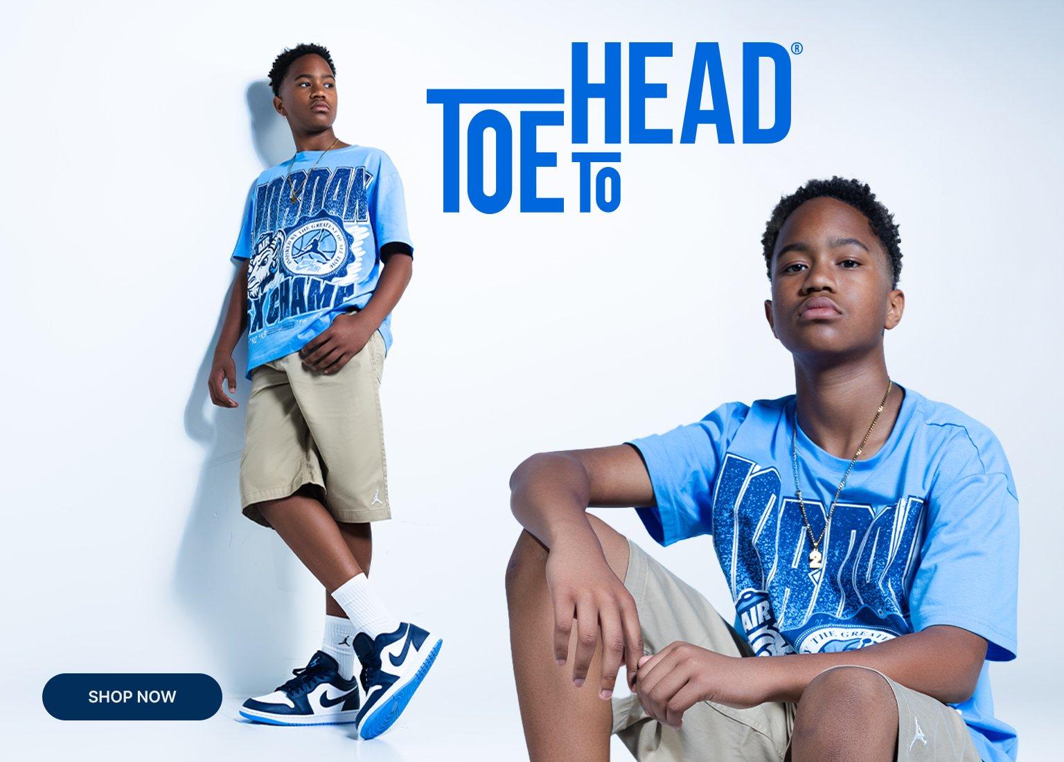 Promotional banner featuring a young boy modeling a light blue Jordan graphic t-shirt and tan shorts, alongside a close-up of dark blue and white Air Jordan 1 Low sneakers with white Jordan crew socks. Blue text reads "TOE TO HEAD," with a "SHOP NOW" button in the bottom-left corner.