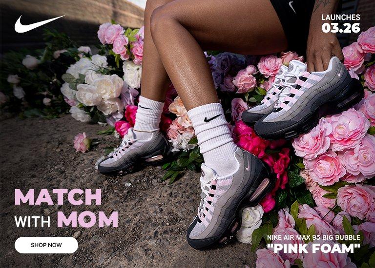 A person wearing Nike Air Max 95 "Pink Foam" sneakers sits among pink and white roses. Text reads "Match with Mom," "Launches 03.26," and "Nike Air Max 95 Big Bubble 'Pink Foam'." A "Shop Now" button and Nike swoosh are also visible.