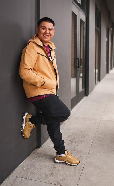 Alex Walter posing against a wall in gold Nike tech fleece and Nike Air Max 97 "golden bullet" shoes