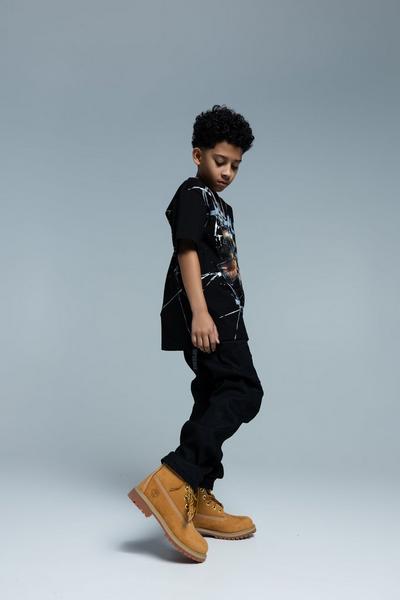 Child wearing a graphic T-shirt, black pants, and classic wheat Timberland boots.