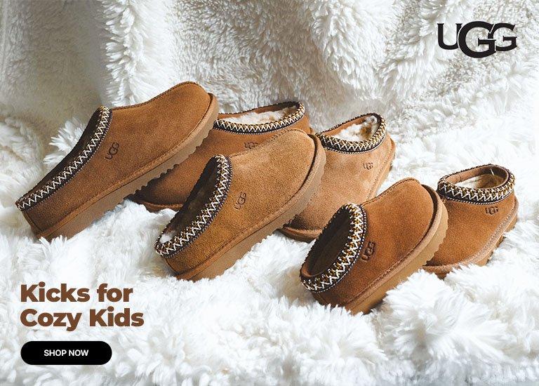 Kids UGG suede slip-on slippers on a soft white faux fur background.