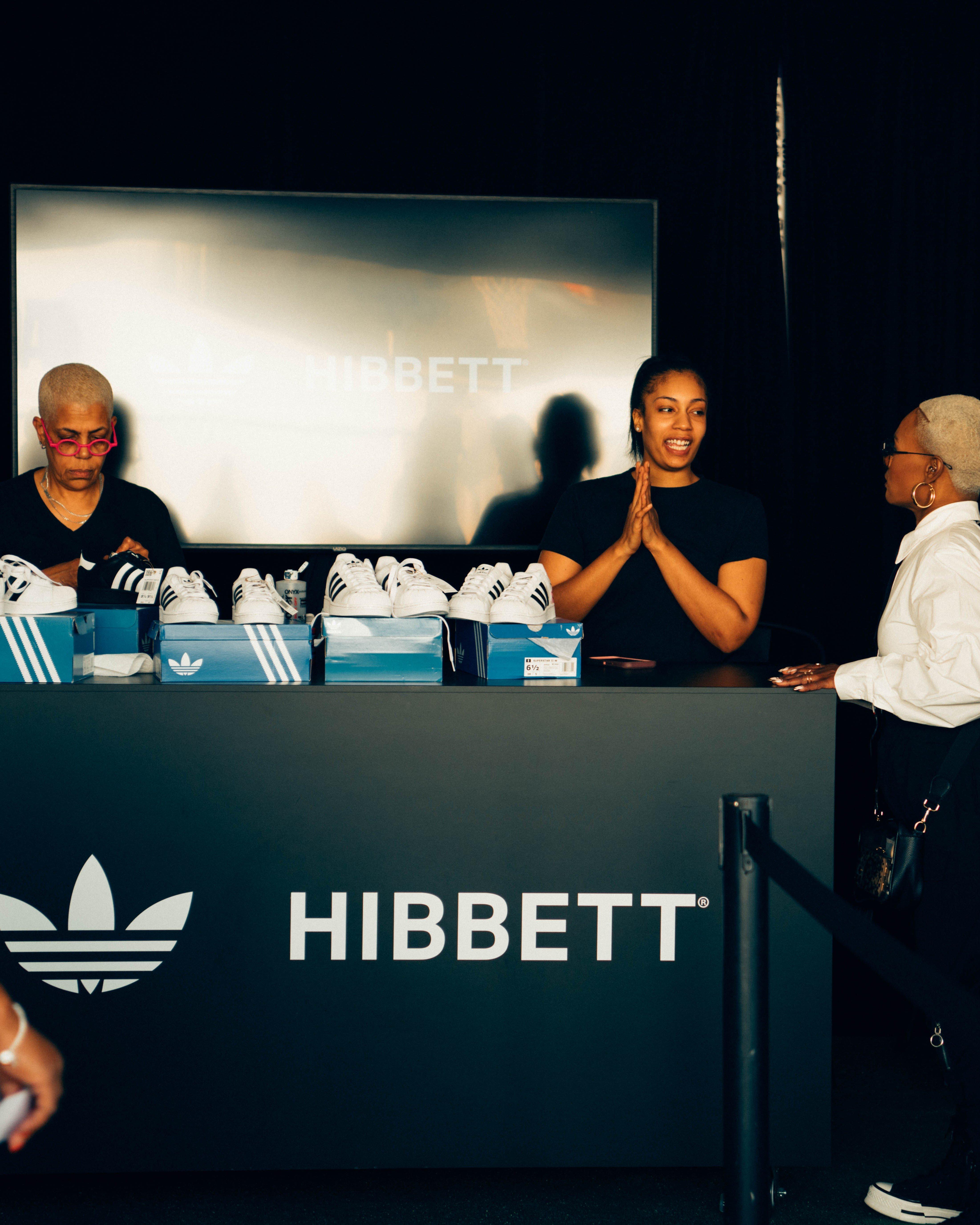 Inside the Hibbett and adidas tent, staff members assist attendees who are browsing the footwear and apparel display.