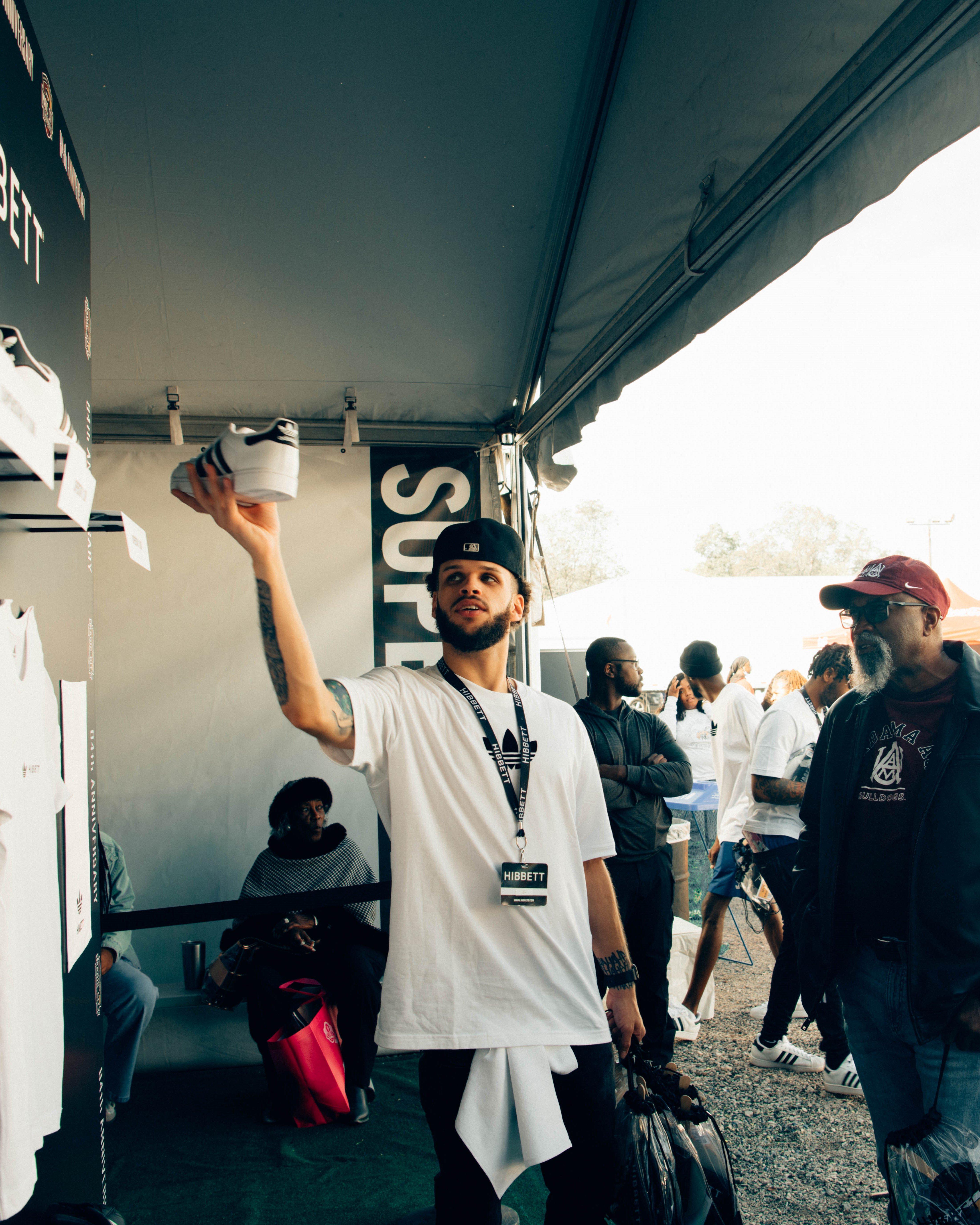 A staff member behind a counter at the Hibbett tent speaks to an attendee, with a clear display of adidas footwear in the background.