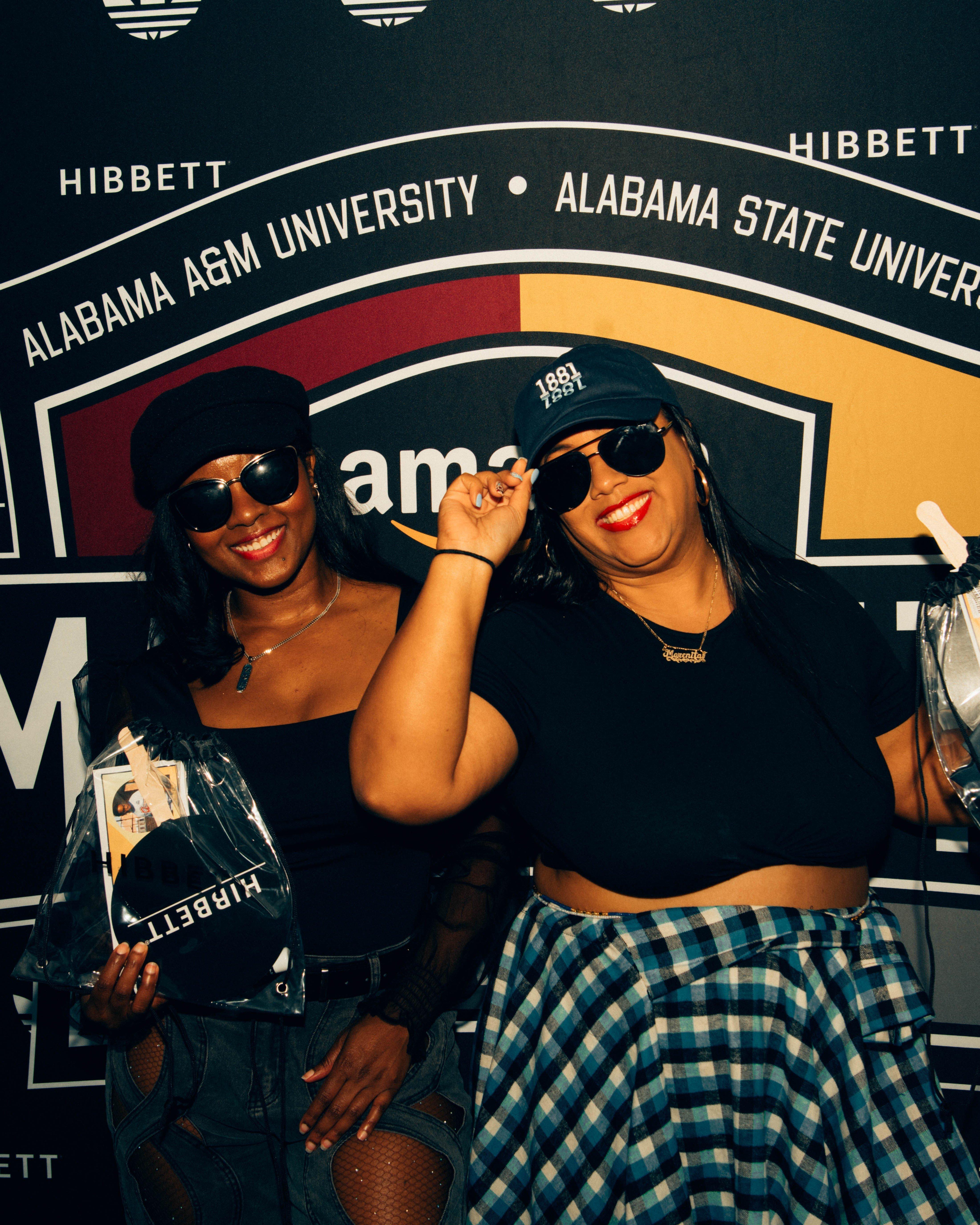 Attendees pose for a photo in front of a branded backdrop inside the tent, which features the logos and colors of Alabama A&M and Alabama State University.