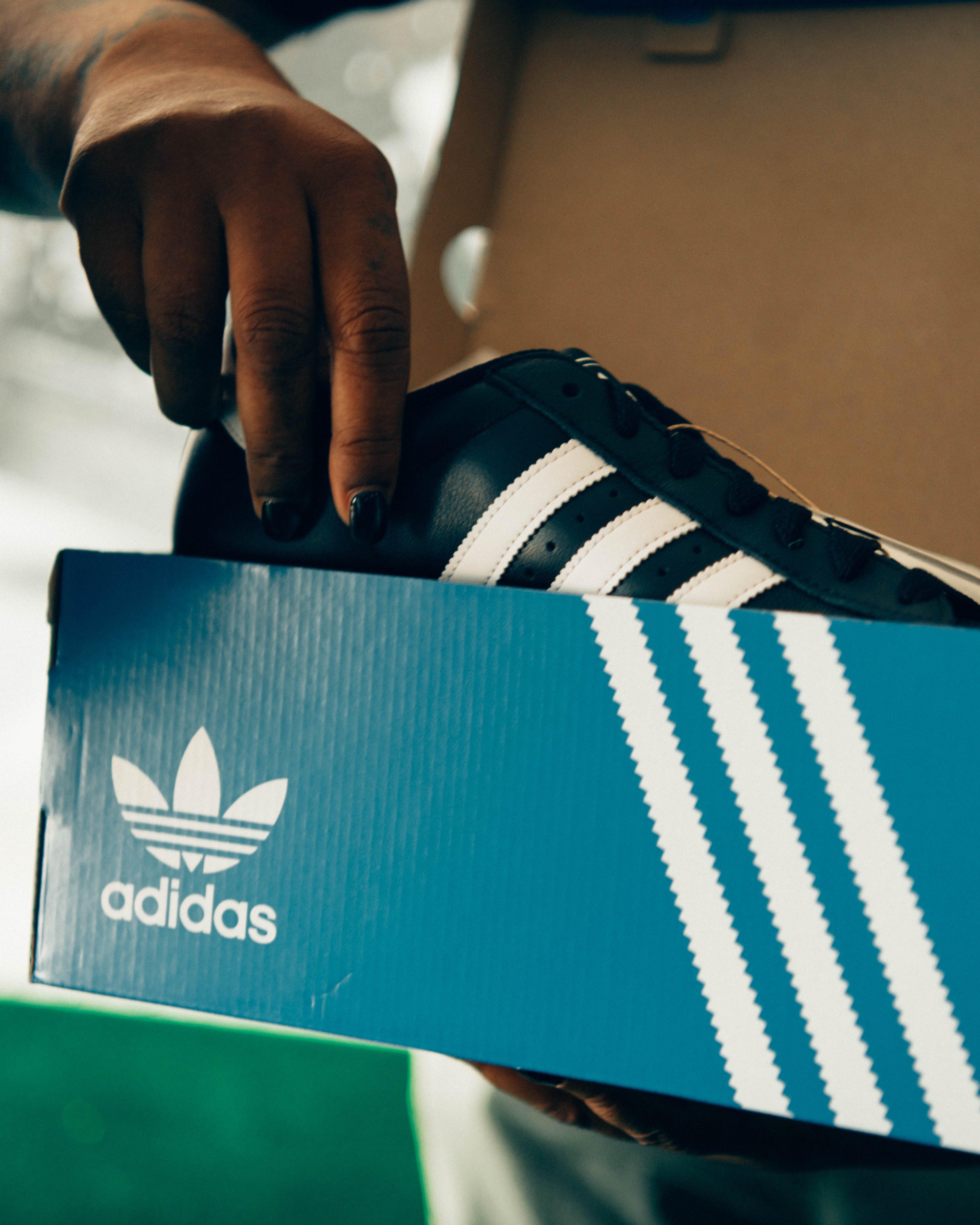 A close-up shot of an attendee's hands pulling a pair of black and white adidas Superstar sneakers out of a blue adidas shoe box.