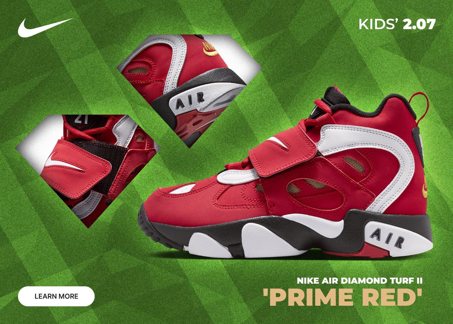 An advertisement for the Nike Air Diamond Turf II Prime Red sneakers. The image features a bold red, white, and black high-top shoe against a textured green turf background. Two diamond-shaped insets show close-up details of the midfoot strap and the heel's AIR branding. The top right corner displays KIDS' 2.07, and a LEARN MORE button is in the bottom left.
