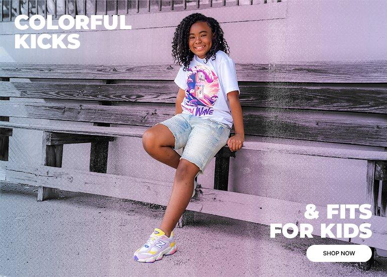 A young girl sits on a wooden bench wearing a white graphic T-shirt, denim shorts, and colorful New Balance 9060 sneakers in pastel shades. The image features a purple color overlay with text that reads "COLORFUL KICKS & FITS FOR KIDS" and a "SHOP NOW" button.