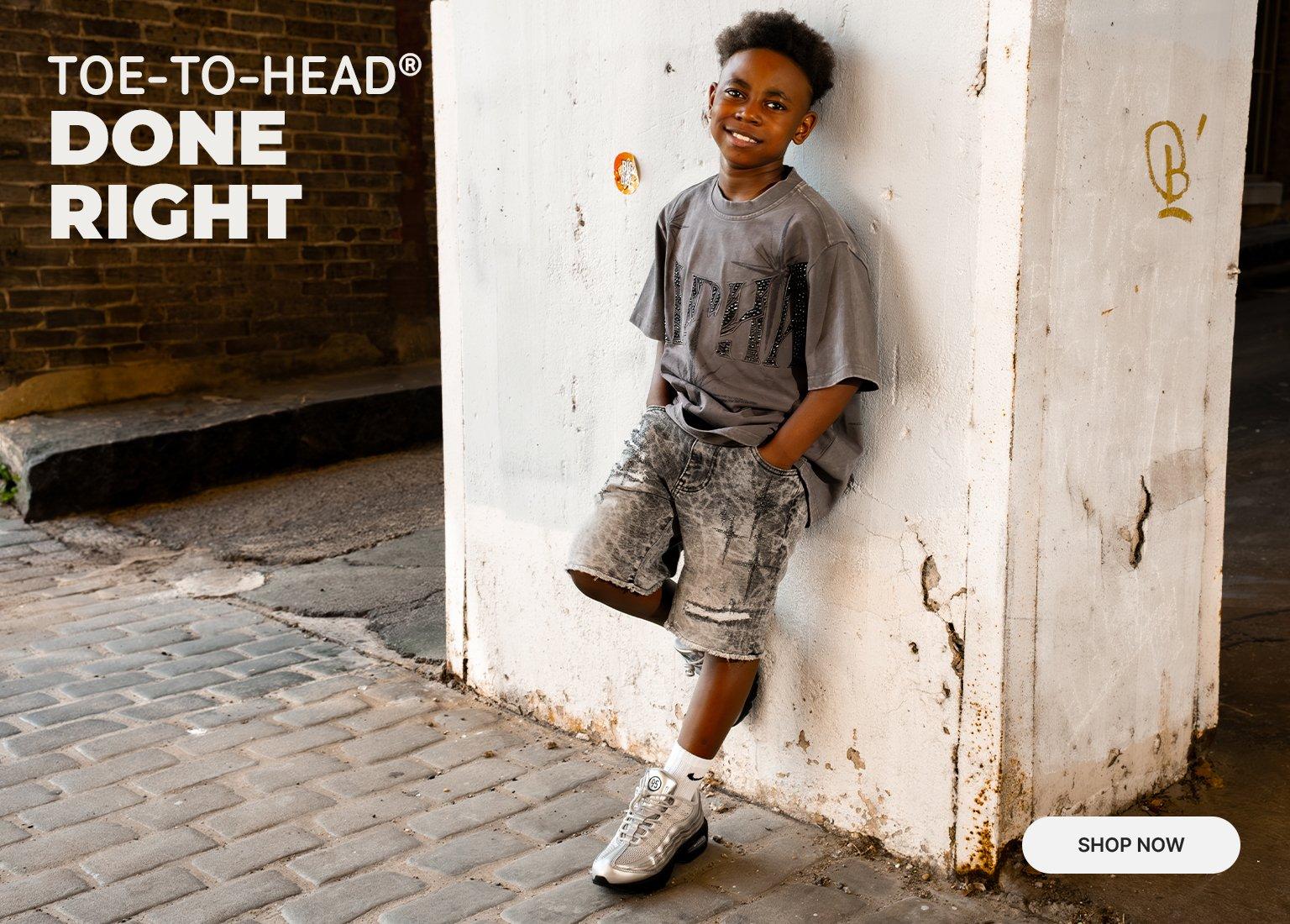 A young boy wearing a charcoal Smoke Rise "Alpha" graphic tee and acid-wash denim shorts leans against a textured white wall. To the right, a close-up focuses on a pair of silver and black Nike Air Max 95 sneakers. The teal text on the left reads "TOE-TO-HEAD® DONE RIGHT" above a "SHOP NOW" button.