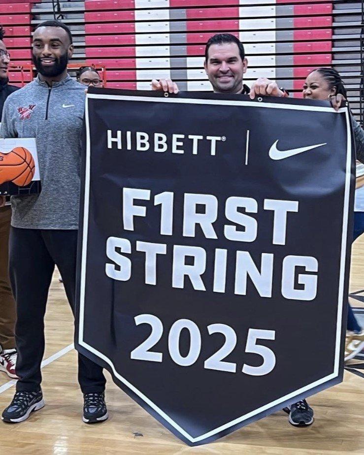 Three representatives standing on the gym court holding a large black banner that reads 'Hibbett | Nike First String 2025'