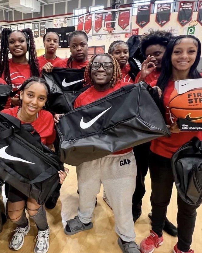 Female student-athletes from the Westwood High School basketball team smiling and holding up new black Nike duffel bags and a First String branded basketball box.