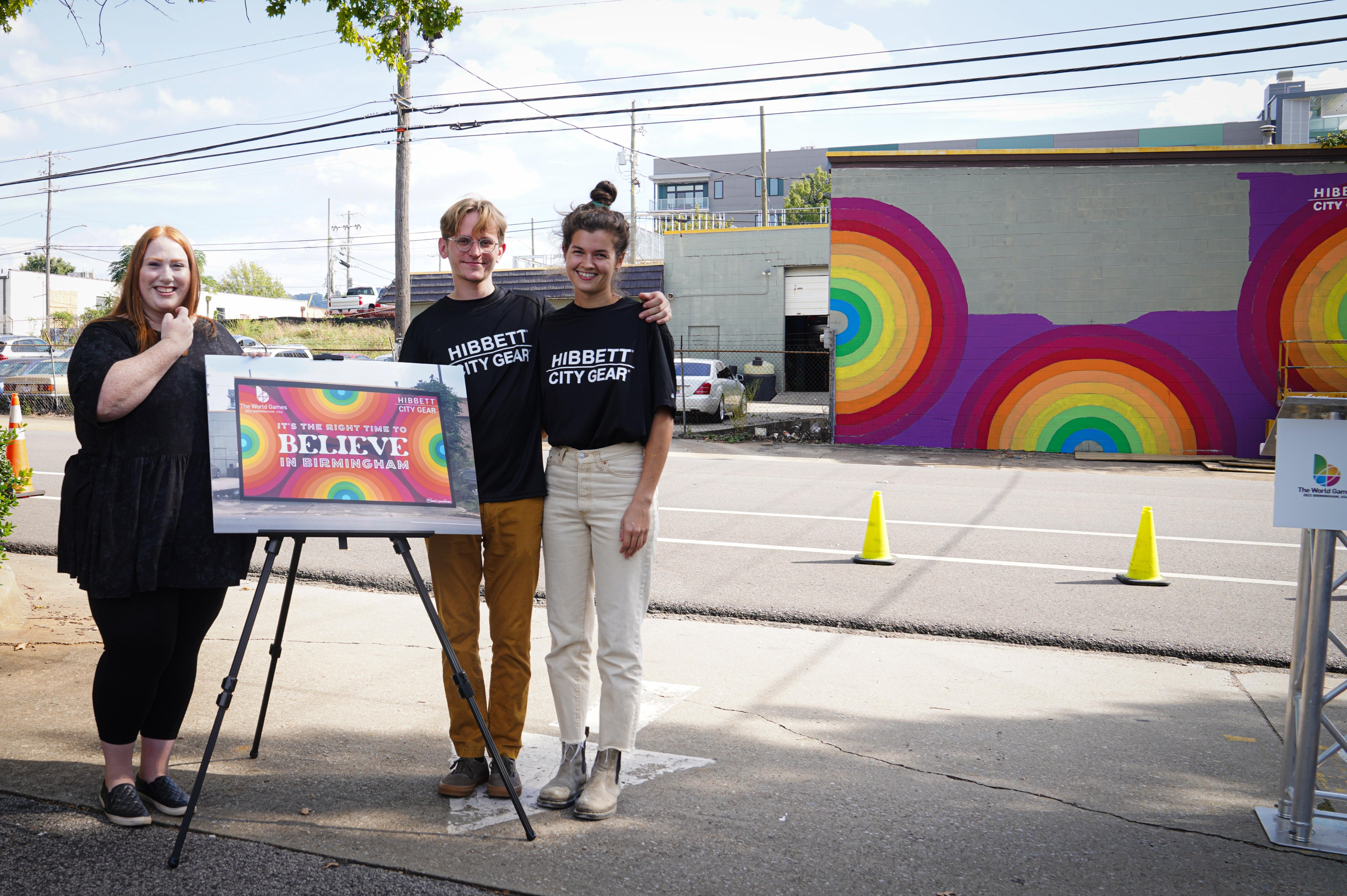 Artist Meghan McCollum with 2 Hibbett employees at the Its The Right Time legacy mural project press conference posing with concept art of future mural.