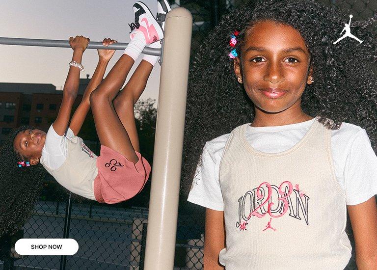 A split-screen image shows a young girl with long, curly hair wearing Jordan brand apparel. On the left, she hangs from a pull-up bar wearing pink shorts and white sneakers with pink accents; on the right, she smiles in a close-up while wearing a cream-colored Jordan 23 tank top over a white t-shirt. A "SHOP NOW" button is in the bottom left corner.