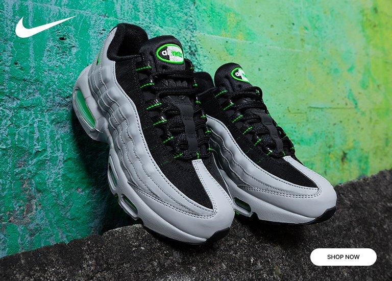 Promotional image of kids’ Nike Air Max 95 sneakers in black and gray with neon green accents, set against a textured green wall.