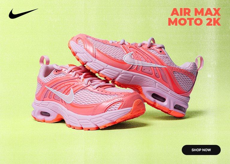 A promotional image for Nike features a pair of Air Max Moto 2K sneakers in a vibrant peach and light purple colorway. The shoes are displayed against a bright lime green textured background, with one sneaker resting slightly on top of the other to showcase the layered mesh and synthetic upper, the white Nike swoosh, and the visible Air unit in the heel. The Nike swoosh logo appears in the top left corner, while the text AIR MAX MOTO 2K is written in bold orange letters in the top right. A black SHOP NOW button is located in the bottom right corner of the frame.