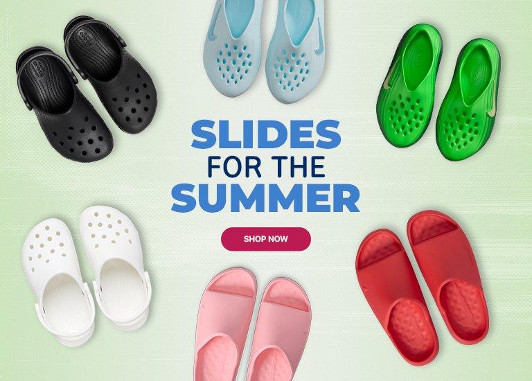 Promotional banner on a light green background featuring six pairs of kids' sandals and slides. The top row shows black Crocs clogs, light blue Nike water shoes, and bright green Nike water shoes. The bottom row displays white Crocs clogs, light pink slides, and red slides. Large blue text on the right reads SLIDES FOR THE SUMMER with a red SHOP NOW button underneath.