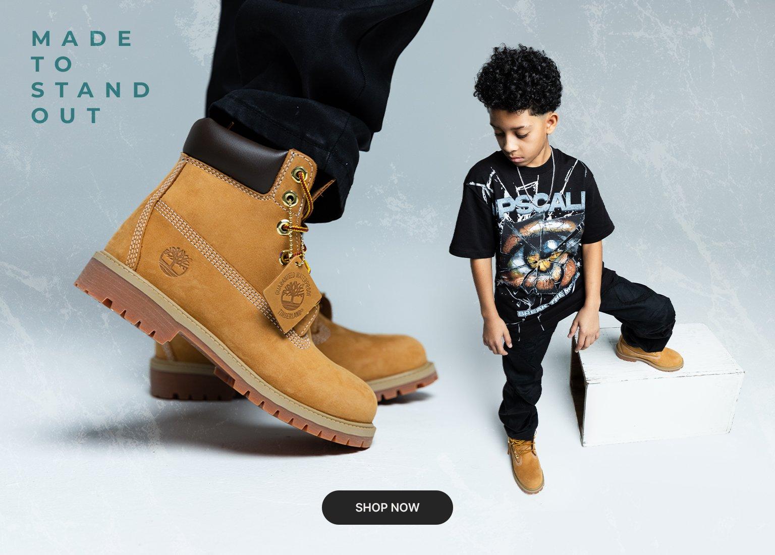 Kids wearing wheat Timberland boots, black graphic T-shirt, and black pants beside oversized Timberland boots with Made to Stand Out text and Shop Now button.