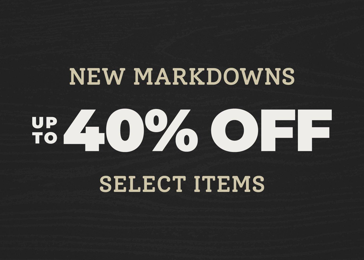 A promotional graphic featuring text centered against a dark wood-textured background. The text reads: "NEW MARKDOWNS" in a tan serif font, followed by "UP TO 40% OFF" in large, bold, off-white block letters, and "SELECT ITEMS" in the tan serif font at the bottom.