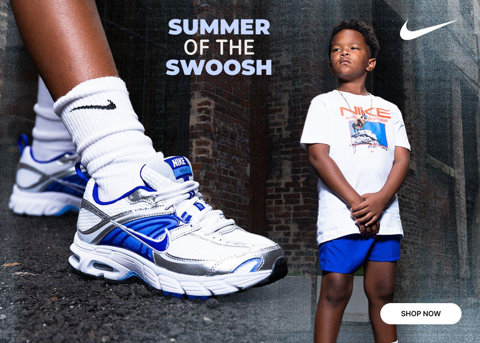 Promotional banner featuring a young boy modeling Nike apparel in an alley alongside a prominent close-up of white, blue, and silver Nike sneakers. Text reads "SUMMER OF THE SWOOSH" with a "Shop Now" button.
