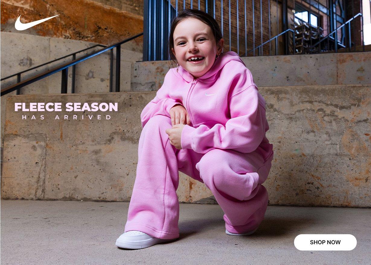 Nike Kids pink fleece hoodie and jogger set with white Nike sneakers and Fleece Season Has Arrived text.