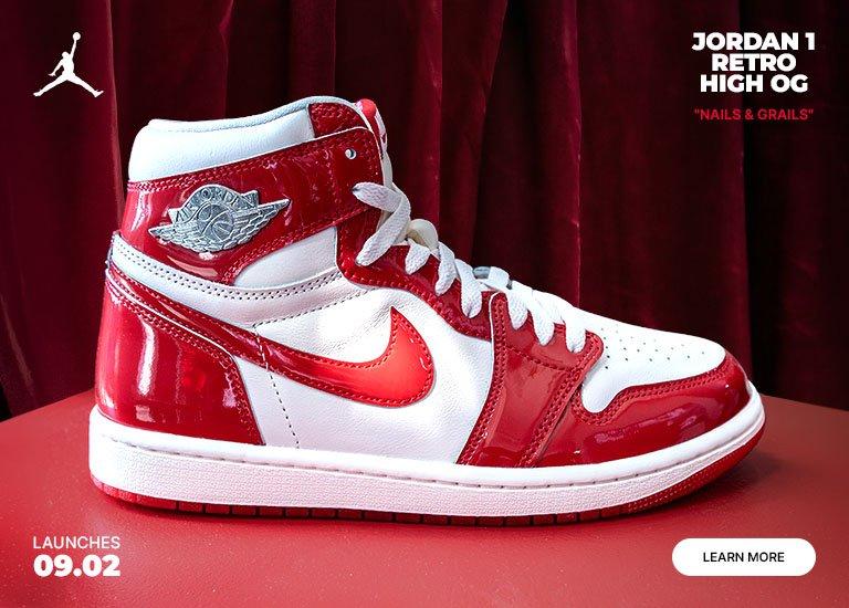 Jordan 1 Retro High OG "Nails & Grails" sneaker in red and white patent leather beside a matching decorative pillow against a red backdrop.