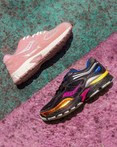  A top-down view of two athletic sneakers placed on a two-toned surface, which is half teal green and half magenta pink. On the top left is a light pink sneaker with a white sole. On the bottom right is a black sneaker with a multi-colored design, including shiny gold, fuchsia, yellow, and blue accents. Both shoes have the Saucony logo on the side.