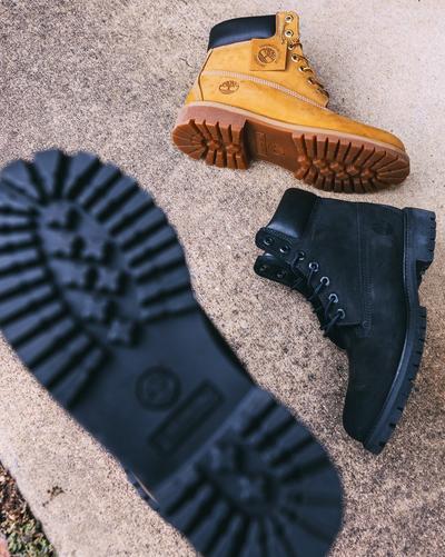 An outdoor shot of a stack of five pairs of Saucony sneakers in various colors, including white, pink, black, and blue. The shoes are resting on a concrete ledge with graffiti on a blue and white background.