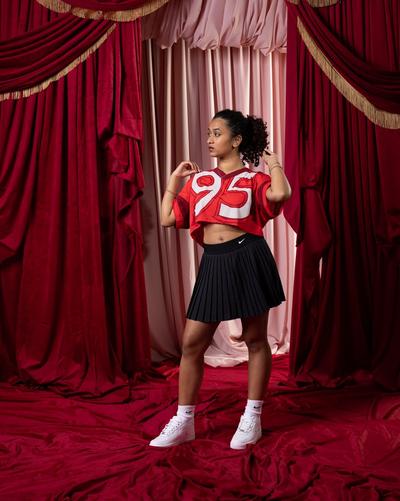 A Woman in Nike jersey, black skirt, and white on white Nike Air Force 1s