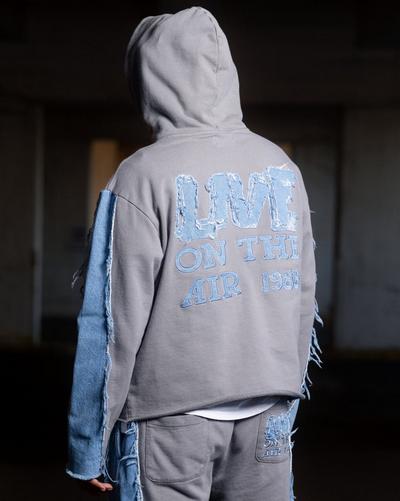 A rear view of a person wearing a grey hoodie with light blue denim patchwork on the sleeves. The back of the hoodie features large, distressed denim letters that read "LIVE ON THE AIR 1988." The matching grey sweatpants also have denim accents and a small branded patch on the back pocket