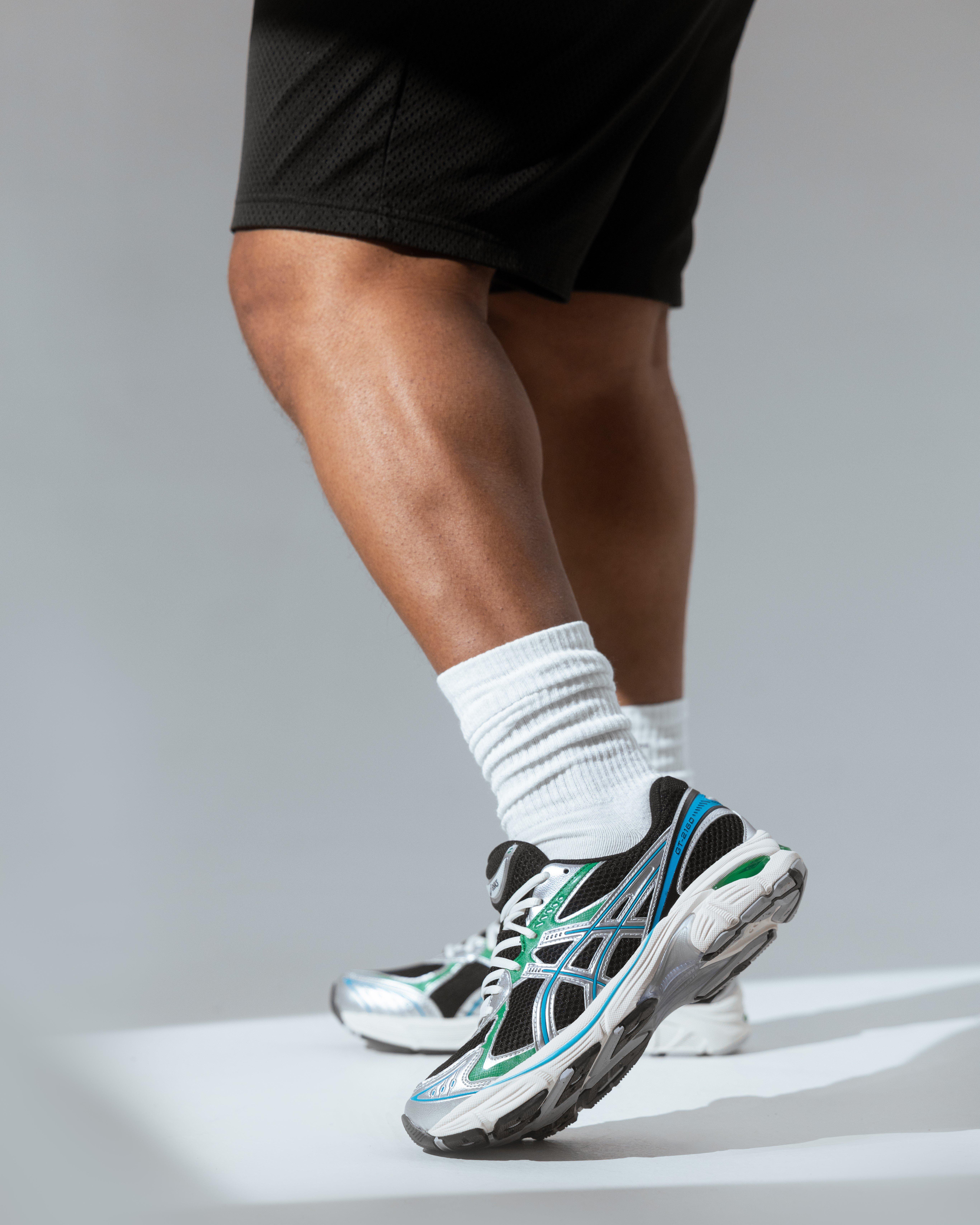  A pair of Asics GEL-2160 sneakers are shown on a concrete staircase. The shoes are white with light green and silver accents.