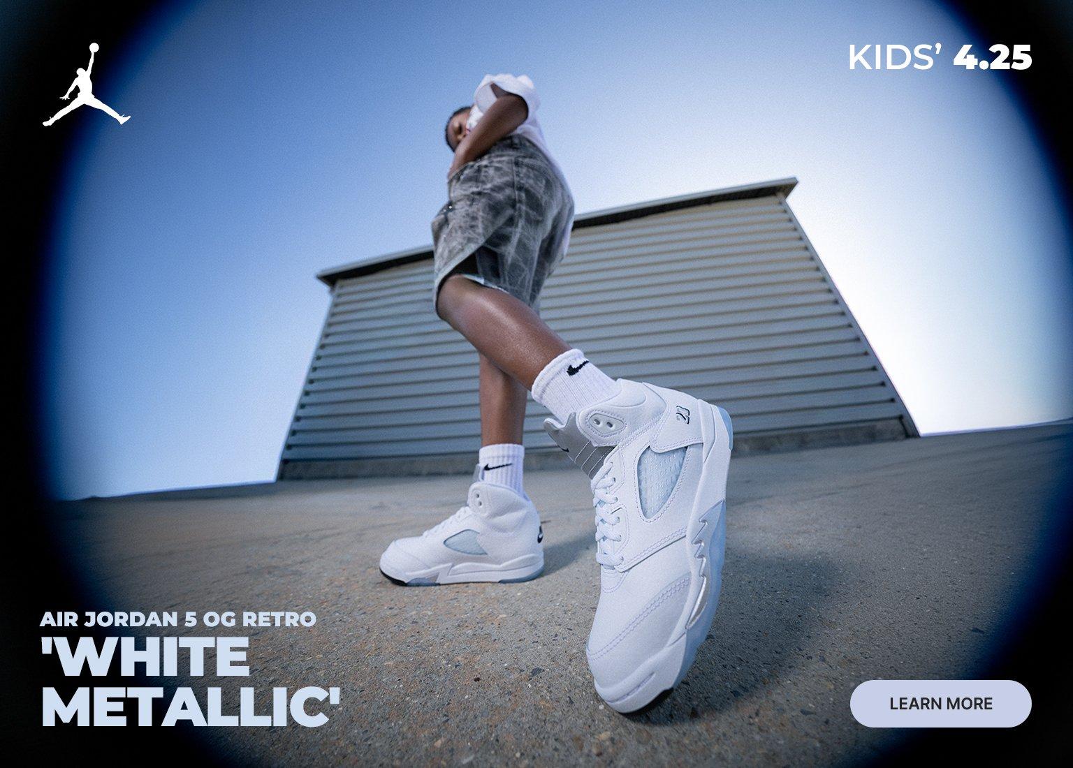 Promotional banner for the Air Jordan 5 OG Retro 'White Metallic' in kids' sizes, featuring a low-angle lifestyle shot of a child wearing the white sneakers and matching Nike socks. The image includes the Jumpman logo, the release date "4.25," and a "Learn More" button.
