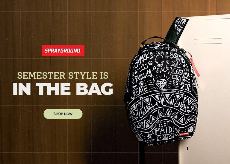 Black Sprayground backpack with white graphic print hanging beside a locker against a wood-paneled background, promoting back-to-school style.