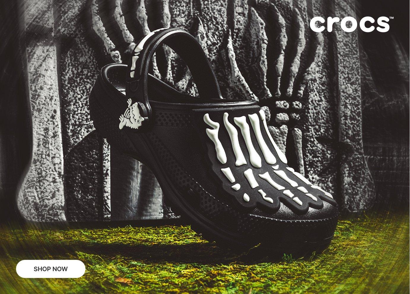 Black Crocs clog with glow-in-the-dark skeleton design in a spooky outdoor setting.