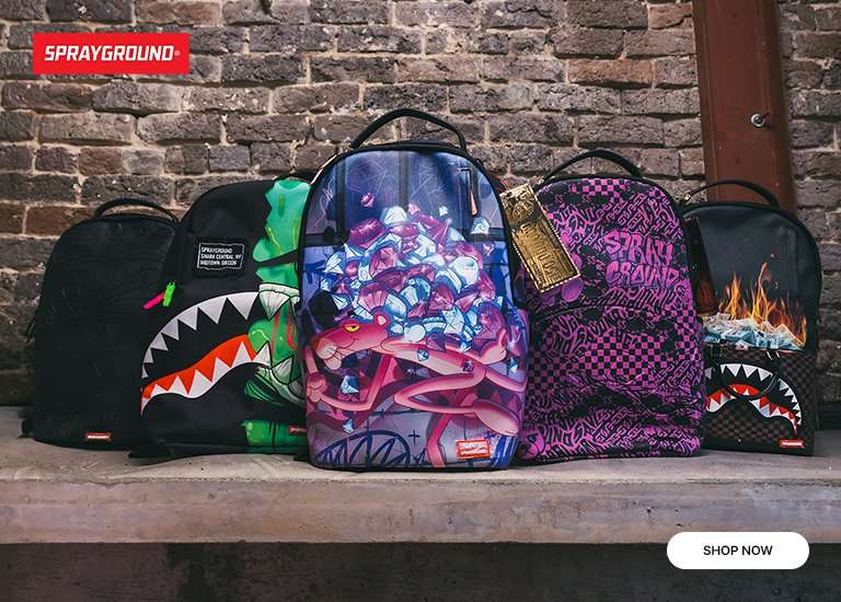 Group of 5 Sprayground Backpacks sitting infront of dark brick wall.
