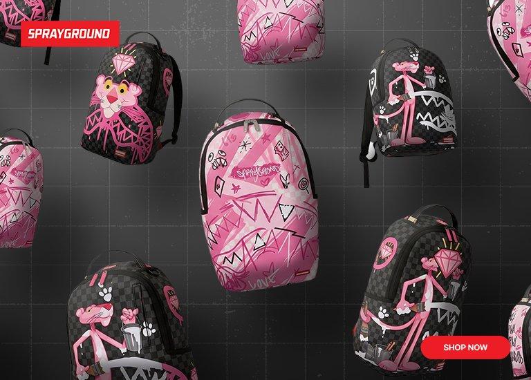 A promotional desktop banner for Sprayground featuring a collection of black and pink backpacks floating against a dark, grid-patterned background. The backpacks showcase graffiti-style graphics, shark mouth patterns, and the Pink Panther character with diamonds. A red "Sprayground" logo is in the top left corner, and a red "Shop Now" button is in the bottom right corner.