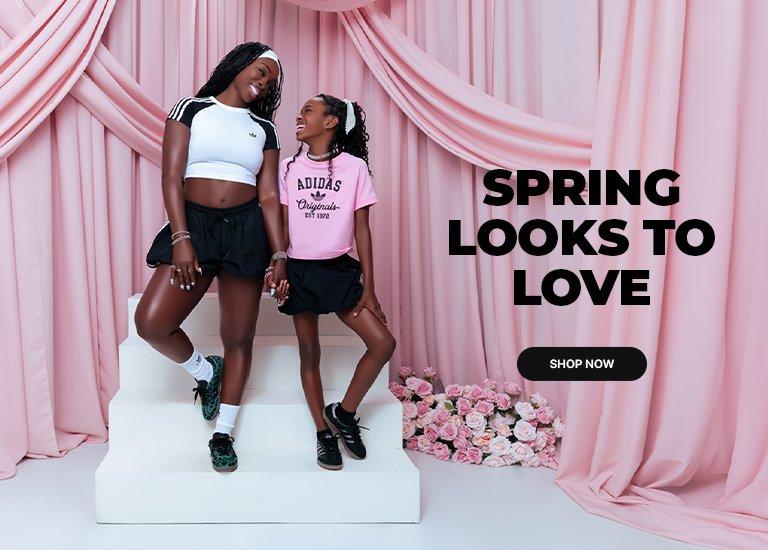 An Adidas promotional banner titled "SPRING LOOKS TO LOVE" featuring a woman and a young girl holding hands and smiling on white steps. They are wearing Adidas apparel, including black shorts and sneakers, against a backdrop of pink draped curtains and roses. A "SHOP NOW" button is visible in the center right.