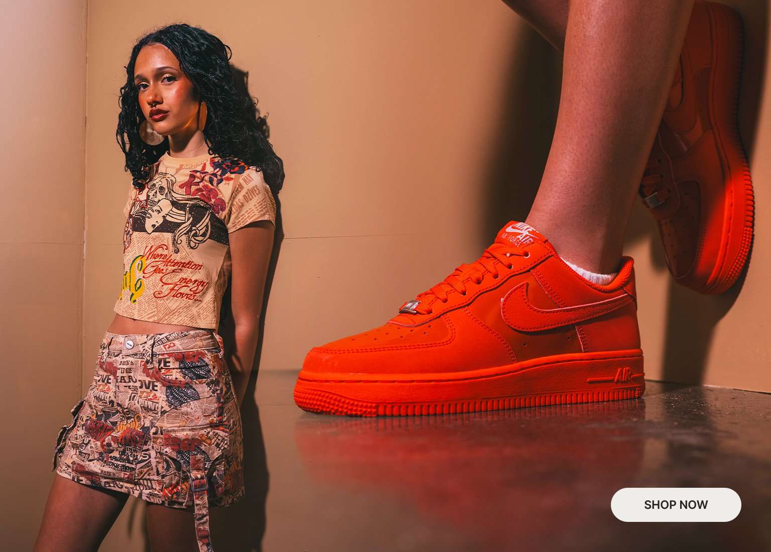 Split lifestyle banner showing a person wearing a printed crop top and matching skirt next to a close-up of bright orange Nike Air Force 1 sneakers, with a “Shop Now” button on the right.