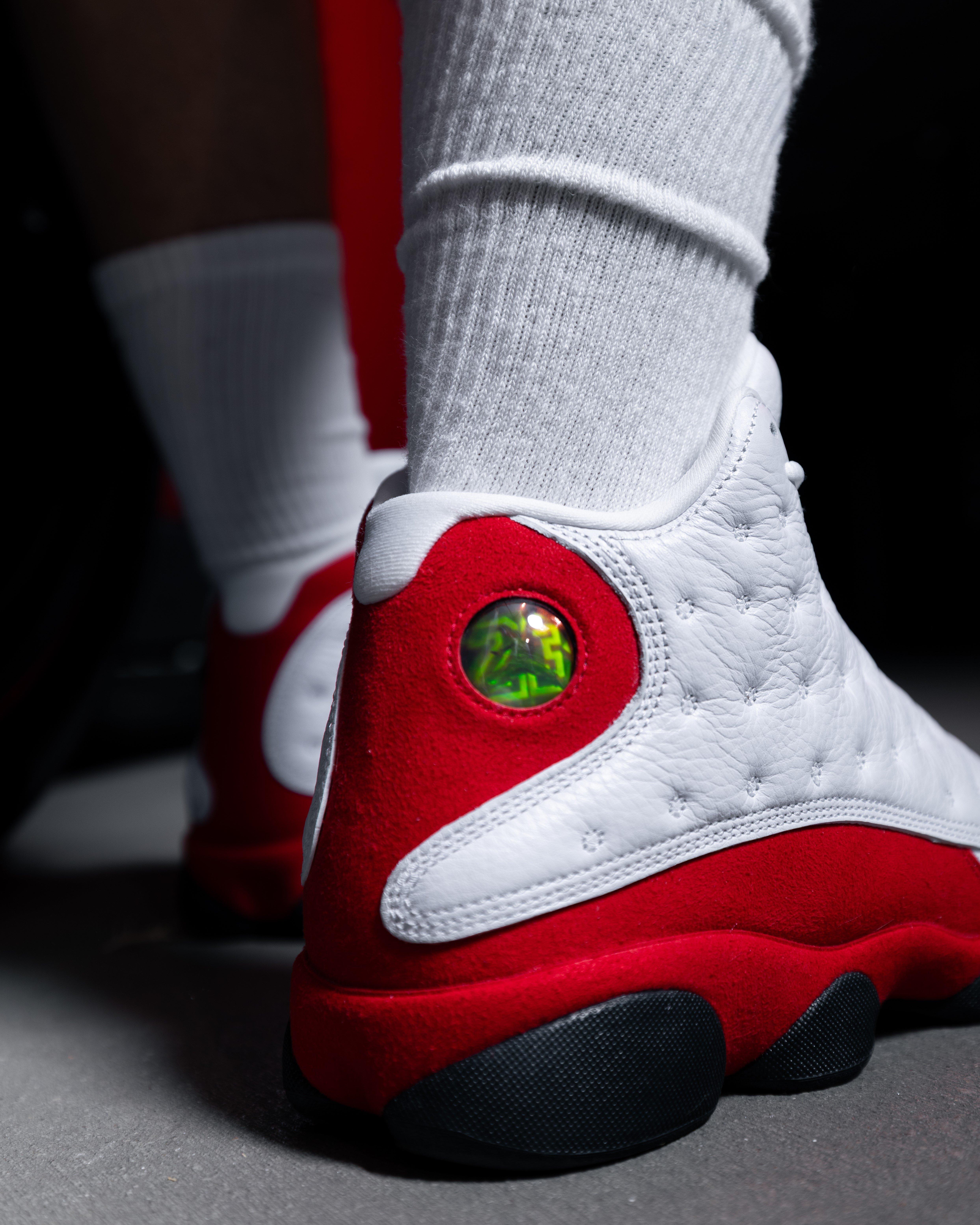 Close-up of the heel of white and red Air Jordan 13 sneakers showing the holographic emblem and red suede panel.