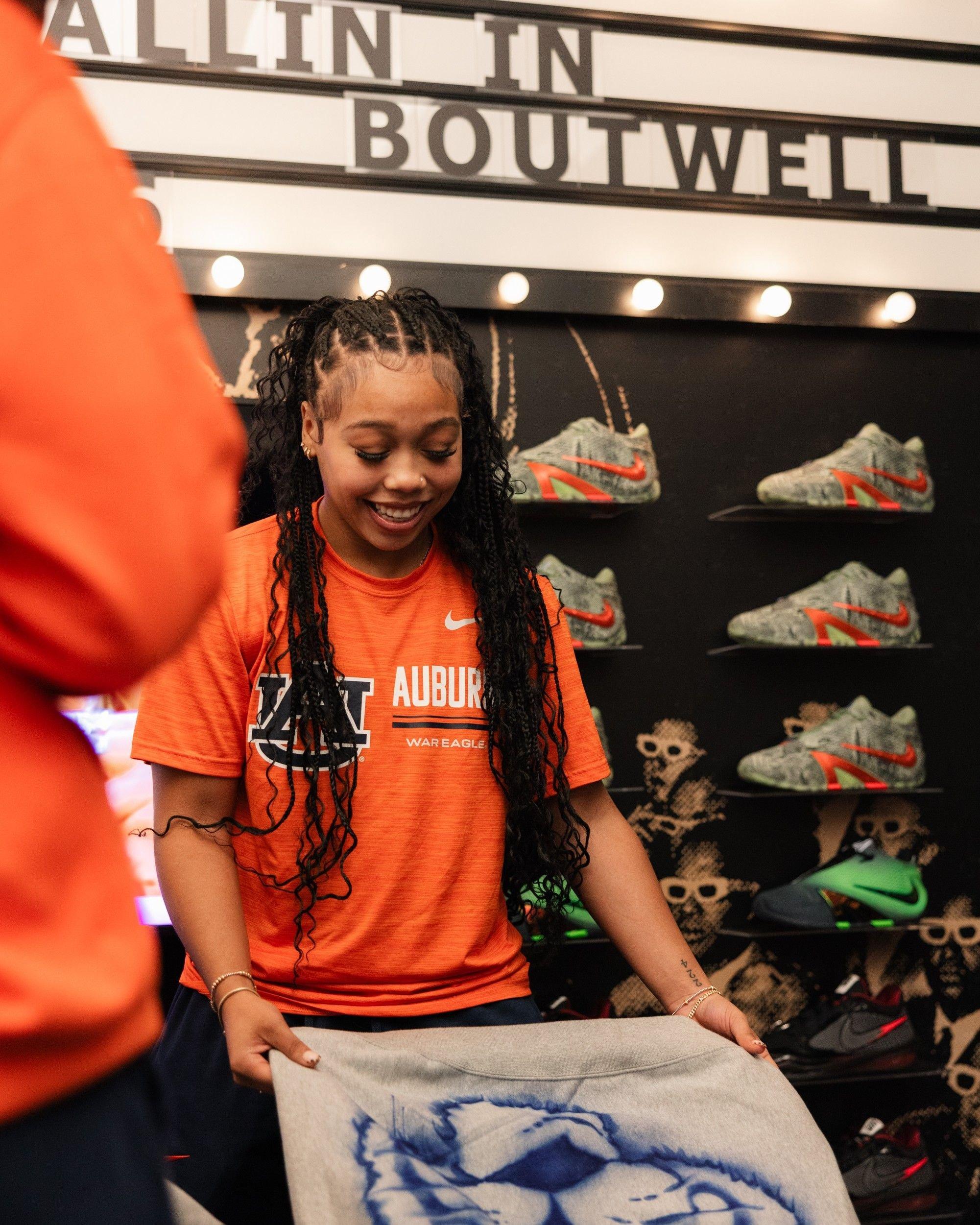 Person in an Auburn T-shirt holds up apparel in front of a Nike sneaker display at Ballin&rsquo; in Boutwell.
