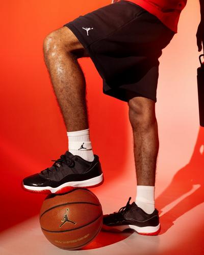 Black Air Jordan 11 Retro Low sneakers with glossy overlays, white midsoles and red outsoles styled with Jordan shorts and socks.