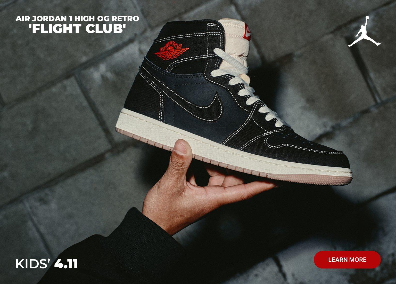 Promotional banner for the Kids’ Air Jordan 1 High OG Retro 'Flight Club.' The image shows a person holding the black, cream, and orange sneakers against a gray stone background, highlighting the heel and side profiles. Text includes a "Learn More" button and a release date of "Kids' 4.11."