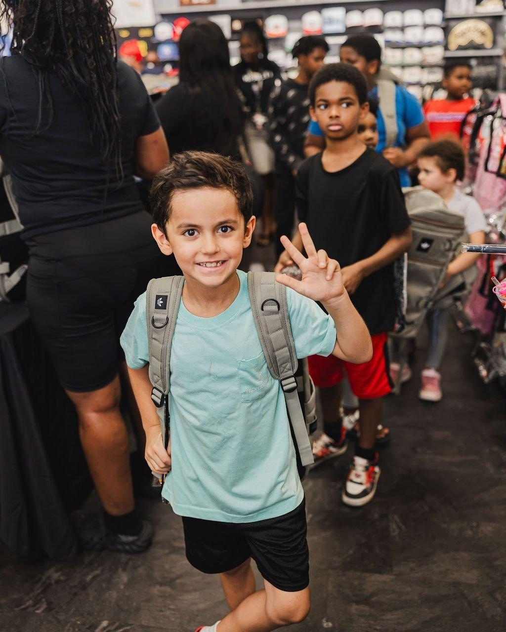 Child wearing a backpack and making a peace sign inside a Hibbett store.