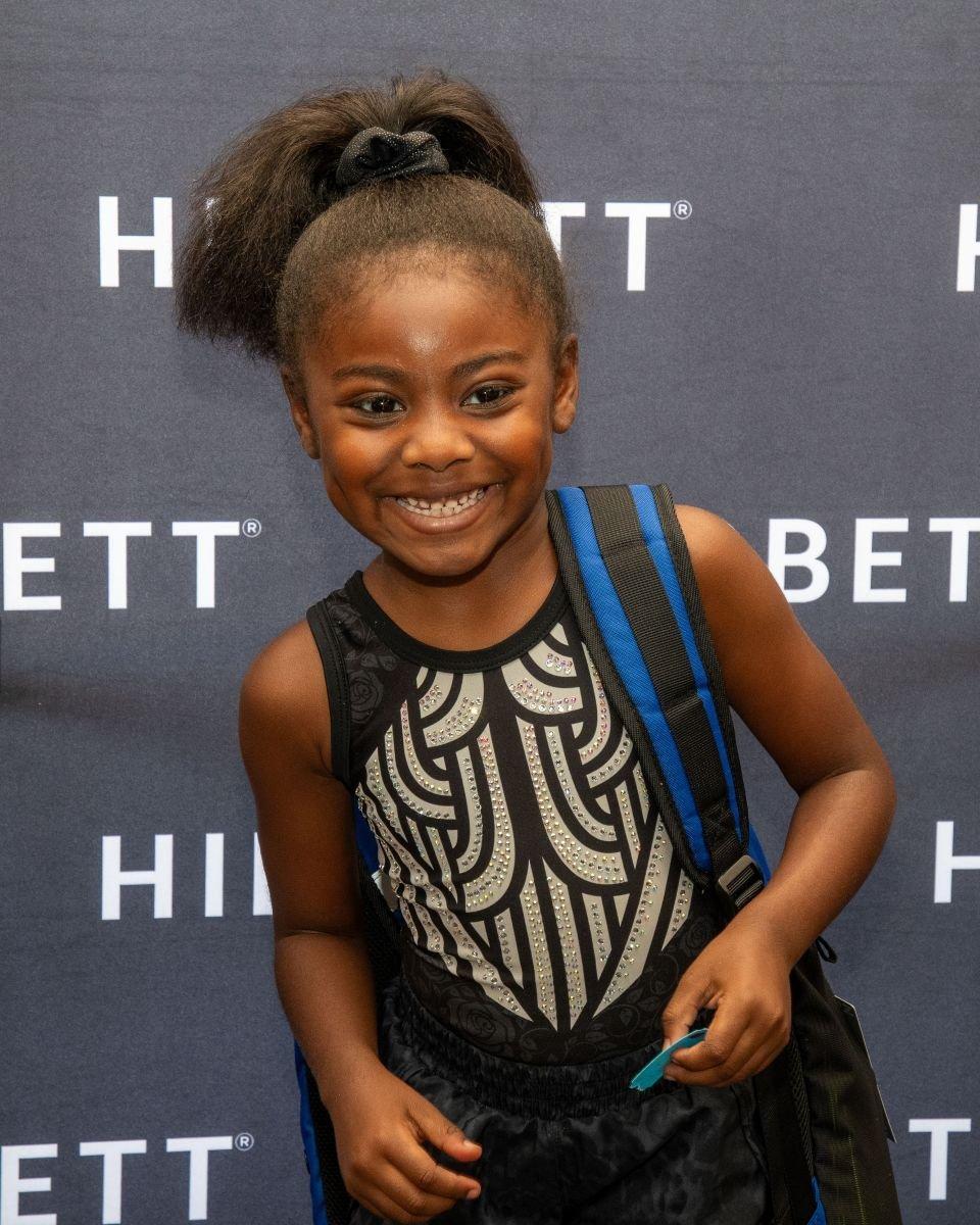 Child wearing a backpack posing in front of a Hibbett backdrop.