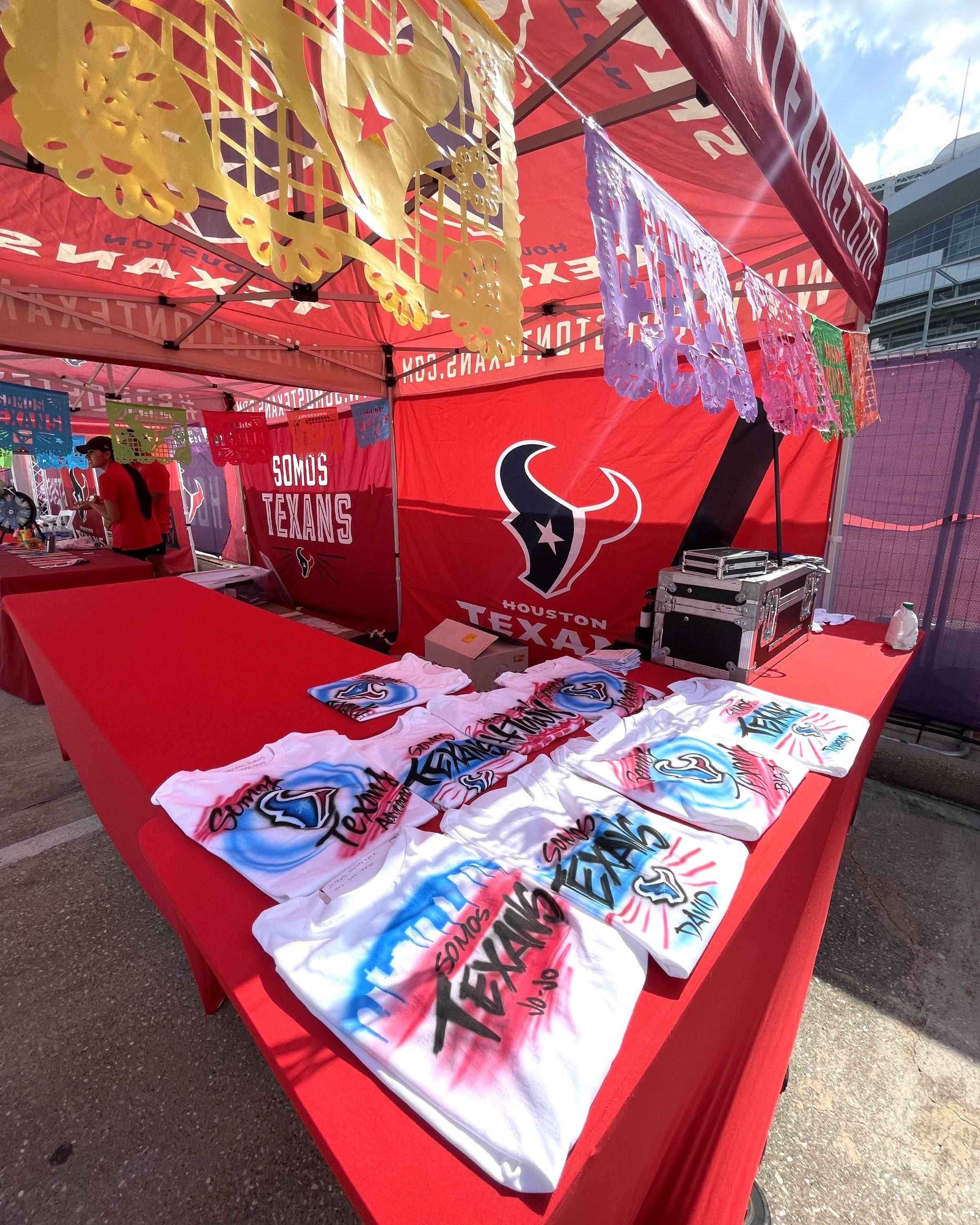 Custom airbrushed Houston Texans shirts displayed at a themed event booth.
