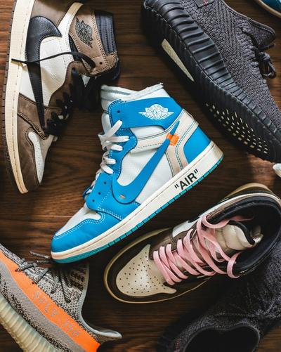 Assorted Air Jordan, adidas Yeezy and Nike sneakers arranged on a wooden surface, including a blue-and-white Off-White Air Jordan 1 at the center.