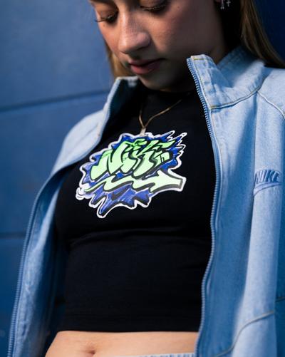 Close-up of a model wearing a black Nike graphic crop top under a light-wash denim zip jacket.