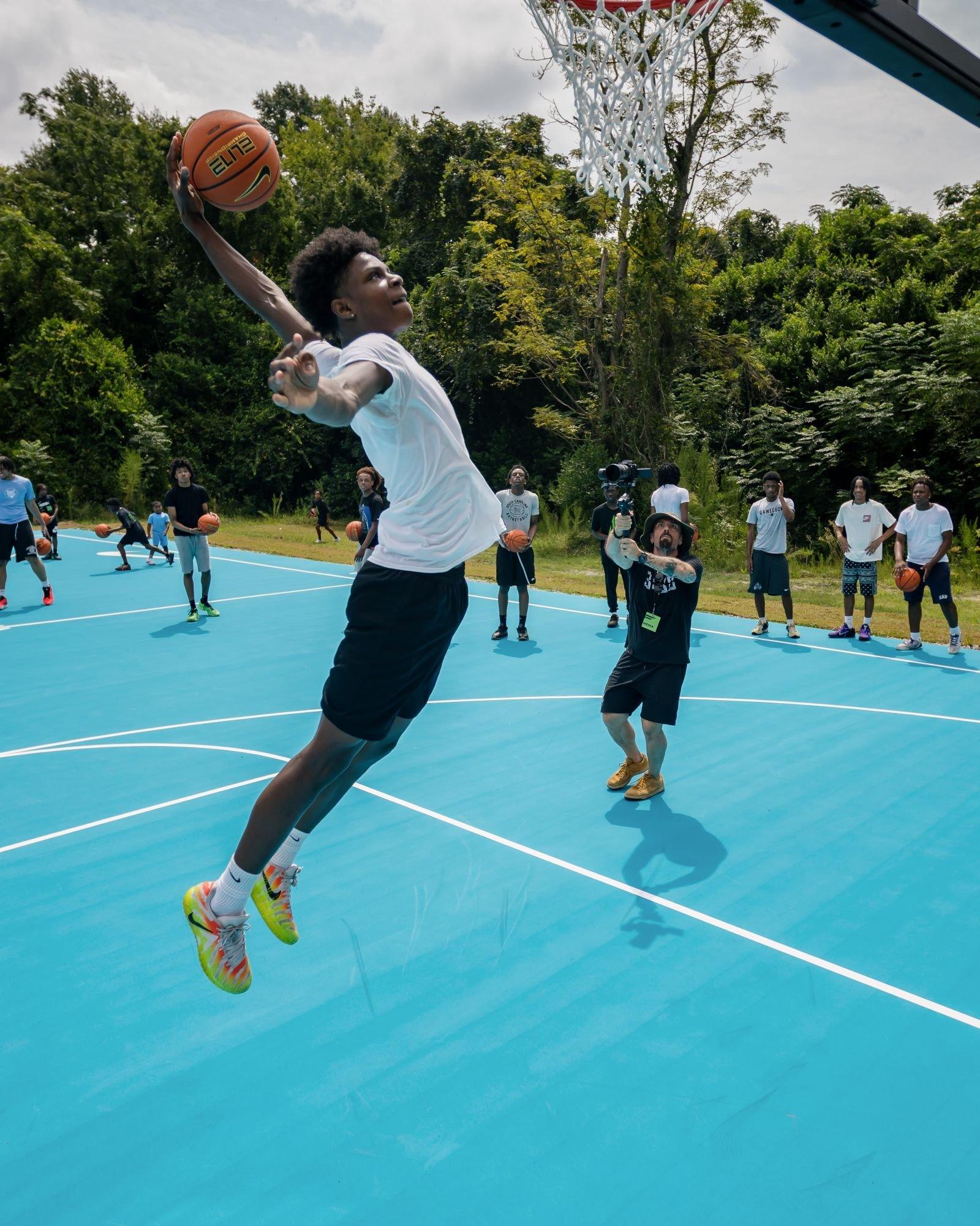 Youth basketball player attempts a dunk on a newly renovated outdoor court during a community basketball event in Sumter, South Carolina.