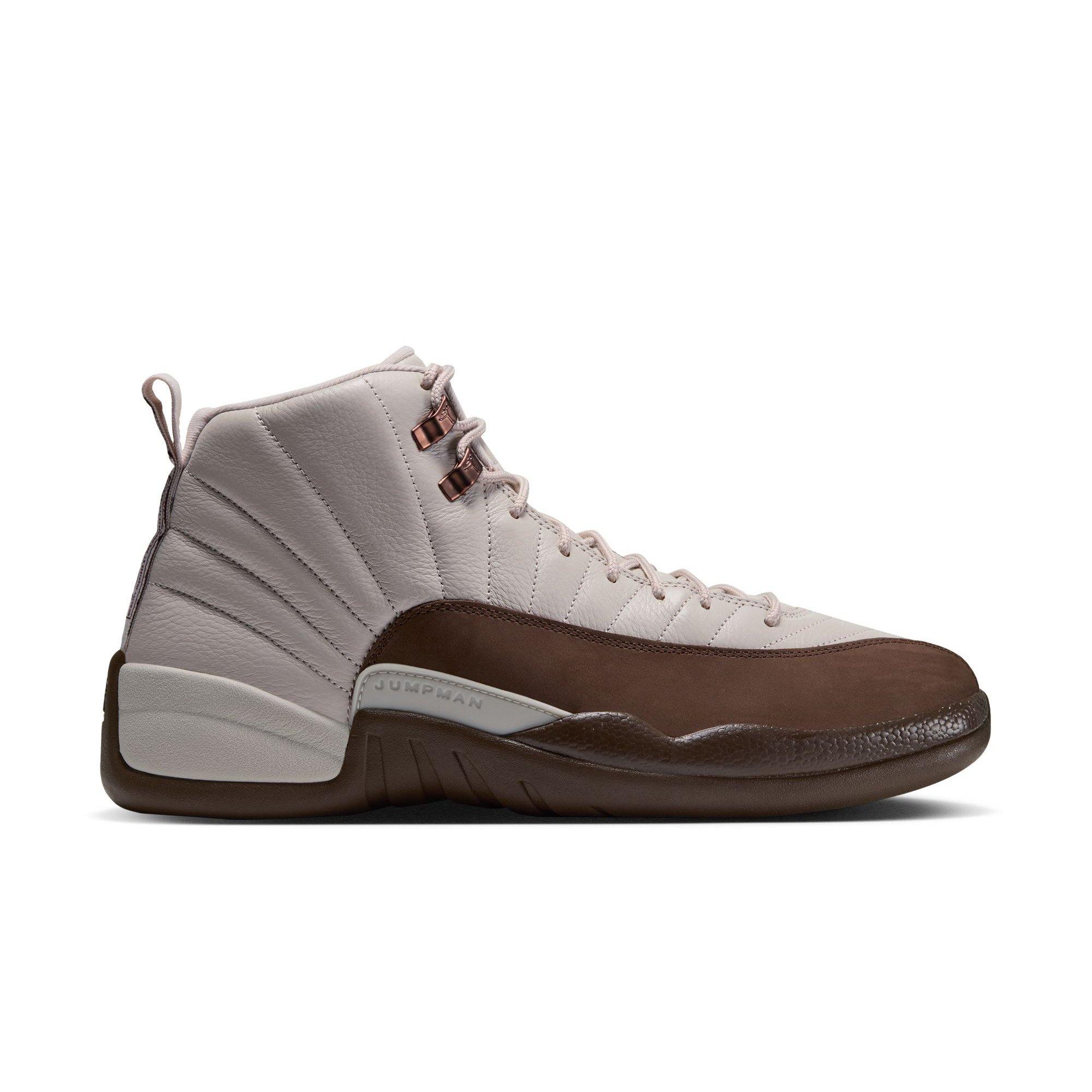 Side view of the Jordan 12 Retro &ldquo;Fireside&rdquo; featuring a cream leather upper, brown mudguard, copper-toned lace hooks, and Jumpman branding.