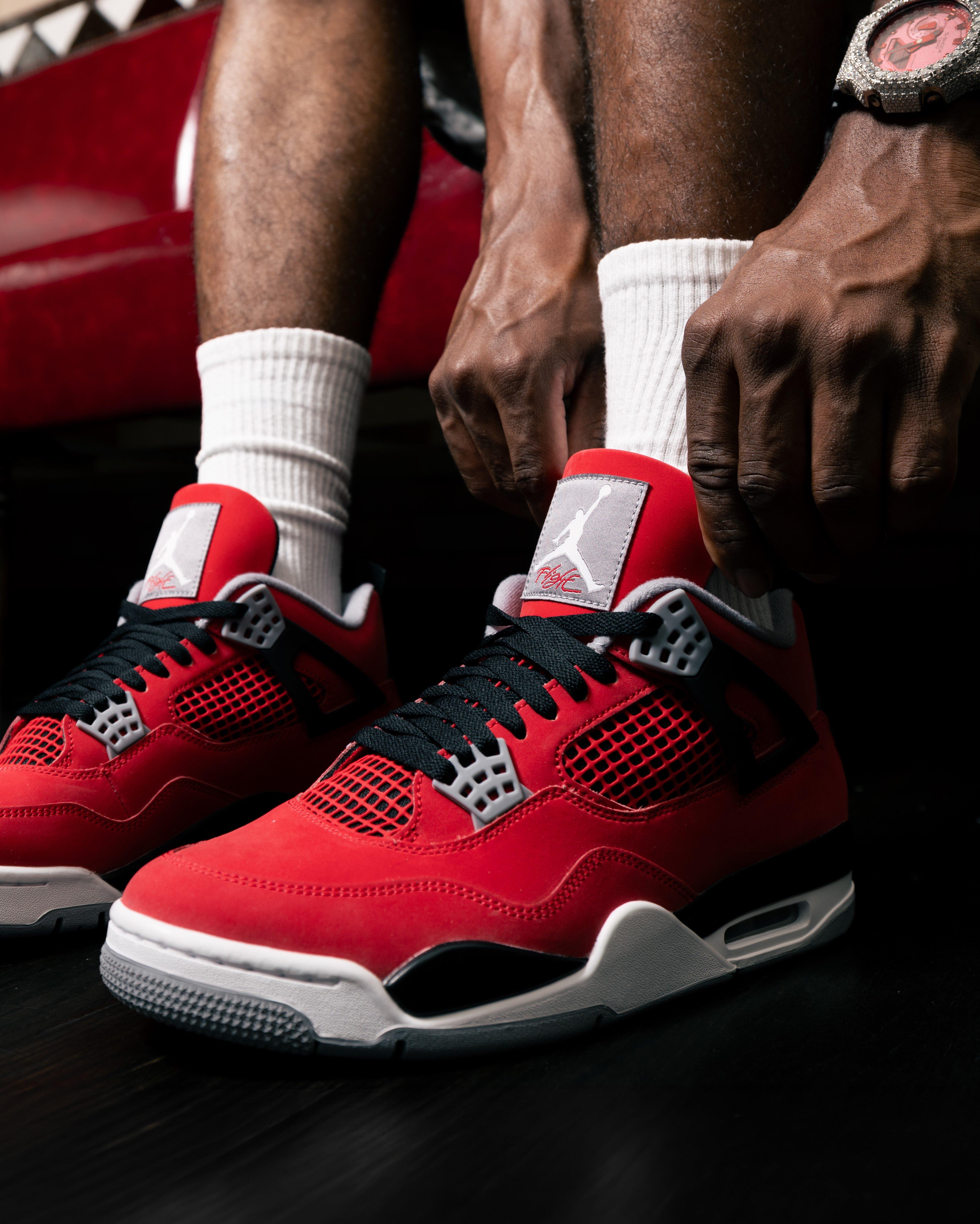 Close-up of hands adjusting laces on red and black sneakers with white socks.